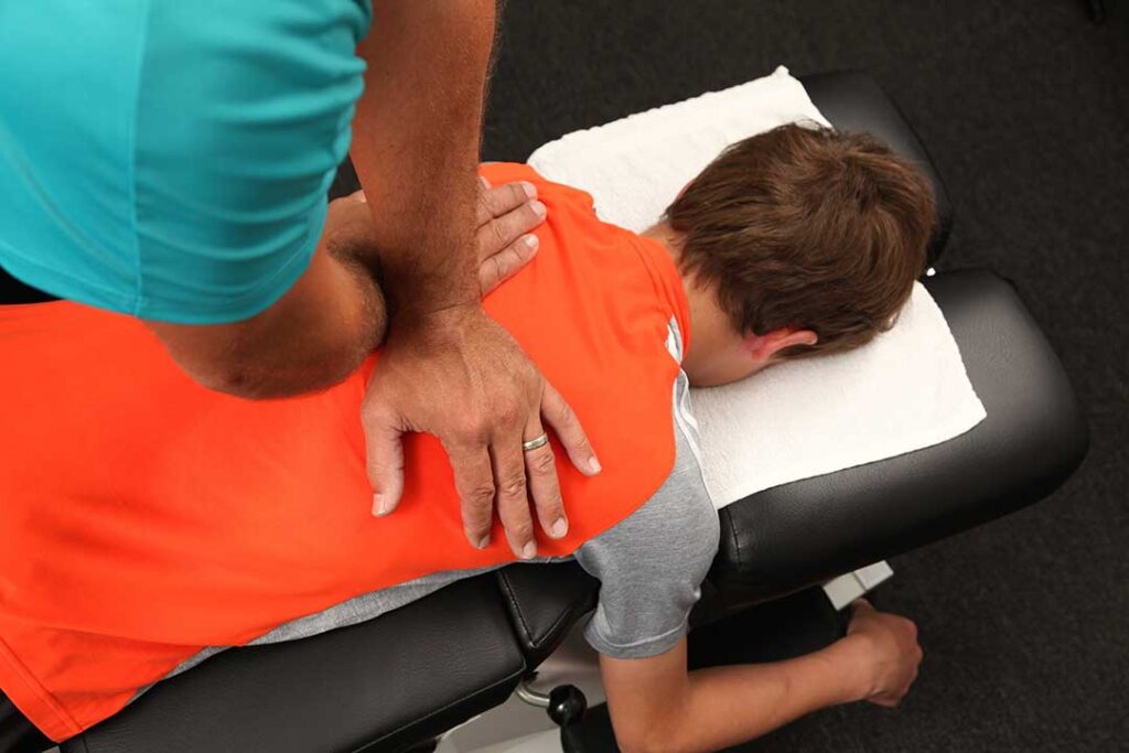 A chiropractor performing a gentle spinal adjustment on an adult patient in a bright outpatient clinic.
