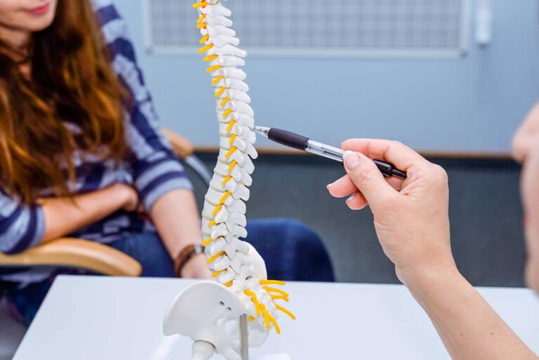 A woman receives a gentle spinal adjustment from a practitioner in a calm clinic setting.