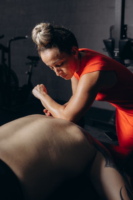 Person gently pressing a tender upper shoulder muscle while seated in a bright room.